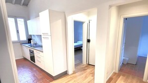 Une cuisine spacieuse, dotée de meubles blancs et d’un plancher en bois, qui donne sur une chambre avec un lit et une salle de bain.