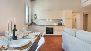 Une cuisine moderne avec des meubles blancs, une table à manger dressée pour le repas et un canapé dans l’espace salon.