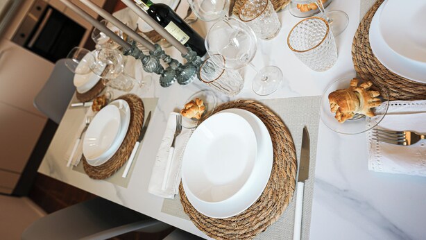 Une table à manger dressée avec de l’assiette blanche, des verres à bord doré et une bouteille de vin.