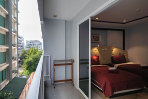 Un balcón con vistas a un paisaje urbano, una cama con ropa de cama roja y un pequeño taburete de madera.
