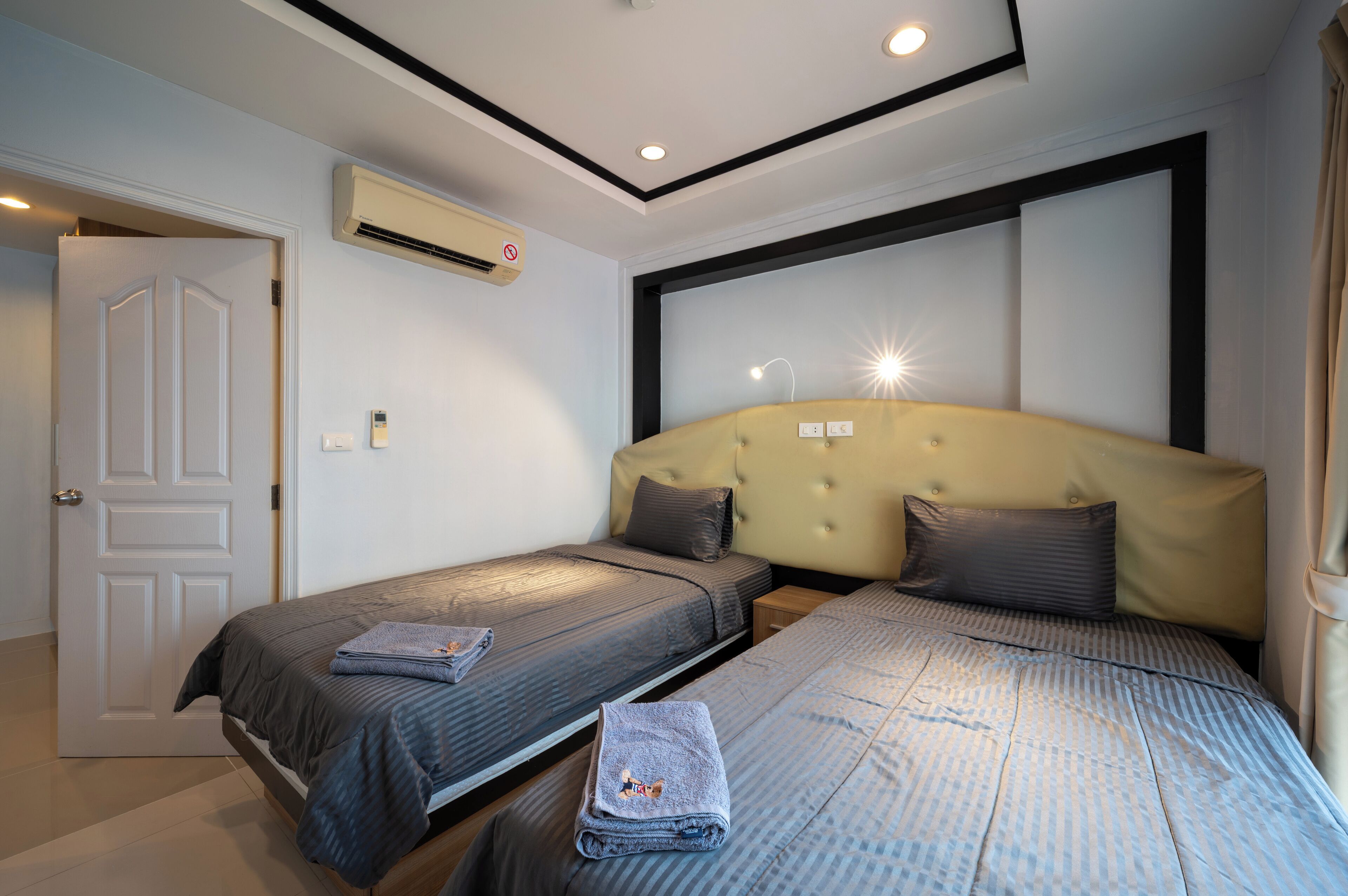 A hotel room with two single beds, a large headboard, an air conditioning unit, and a door.