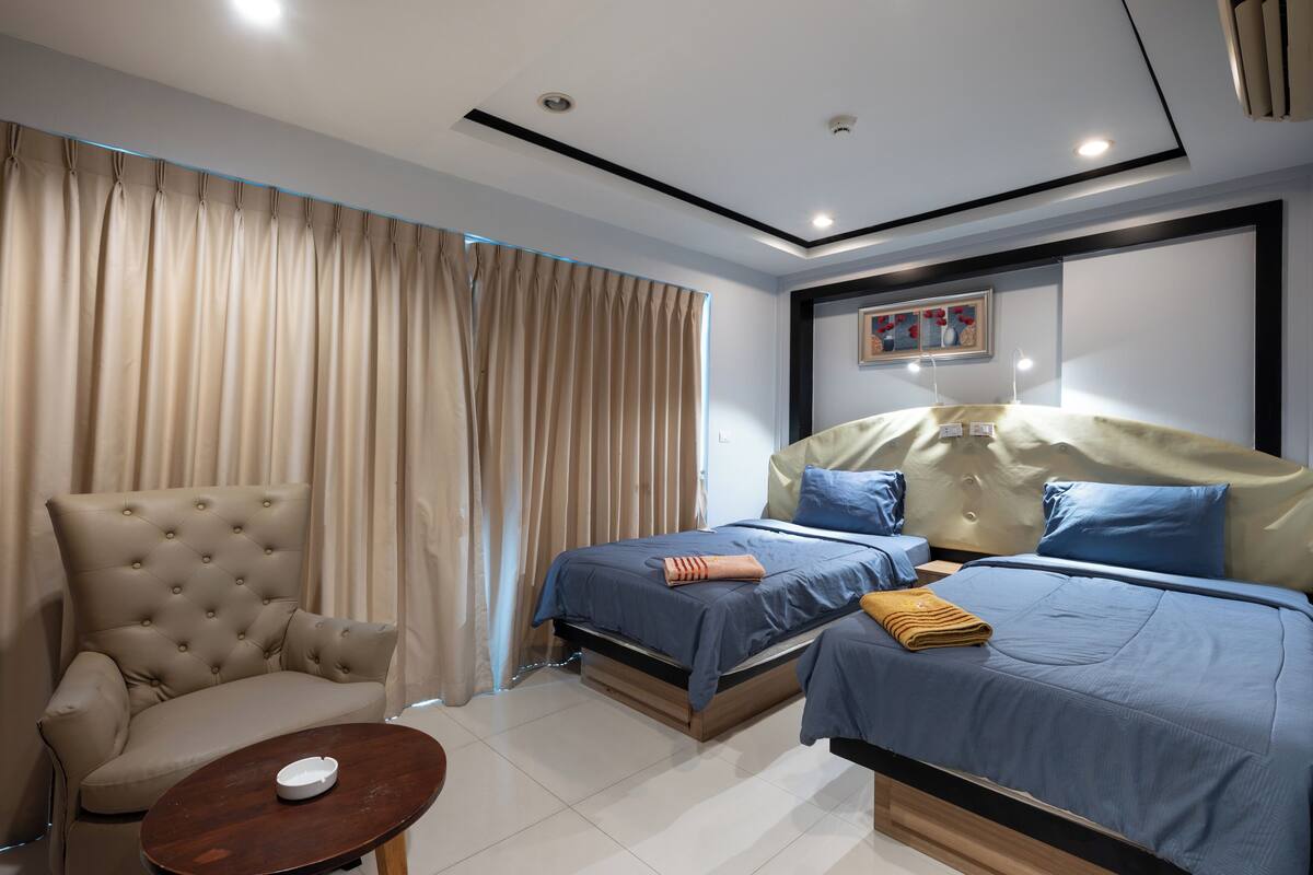 Habitación de hotel con dos camas, un sofá, una mesita y una lámpara en el techo.