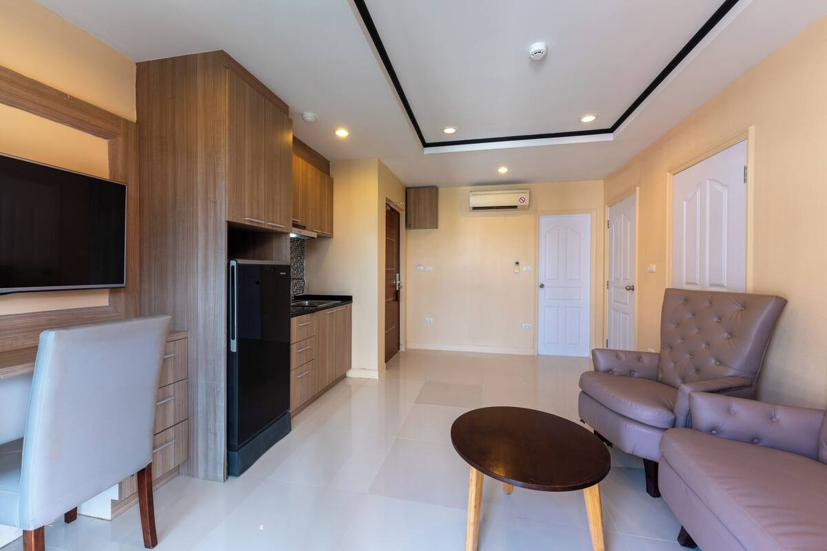 Una sala de estar moderna con un sofá, una mesa de comedor y una zona de cocina con televisor y electrodomésticos.