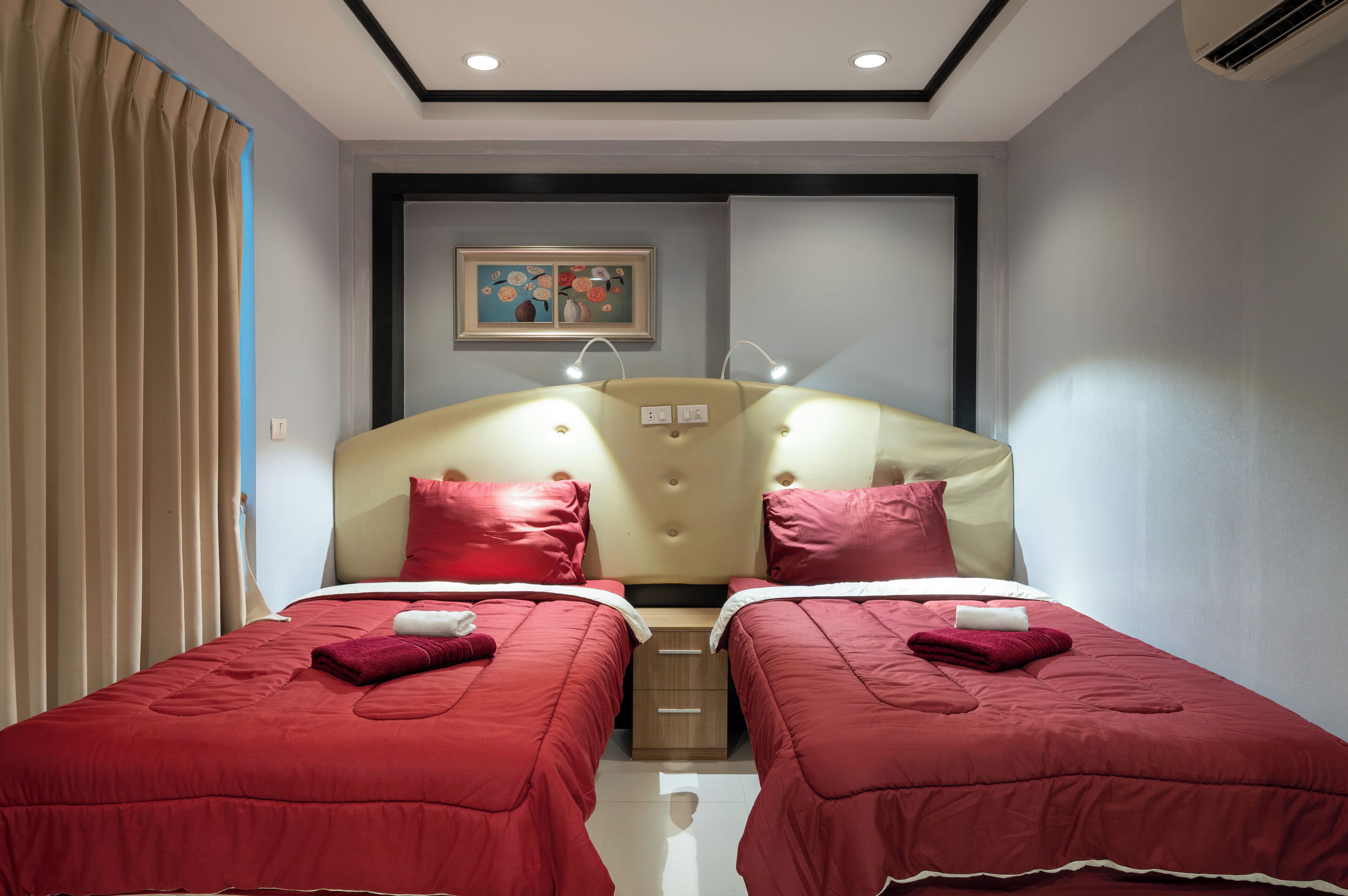A hotel room with two single beds, a headboard with integrated lighting, a bedside table, and a painting on the wall.