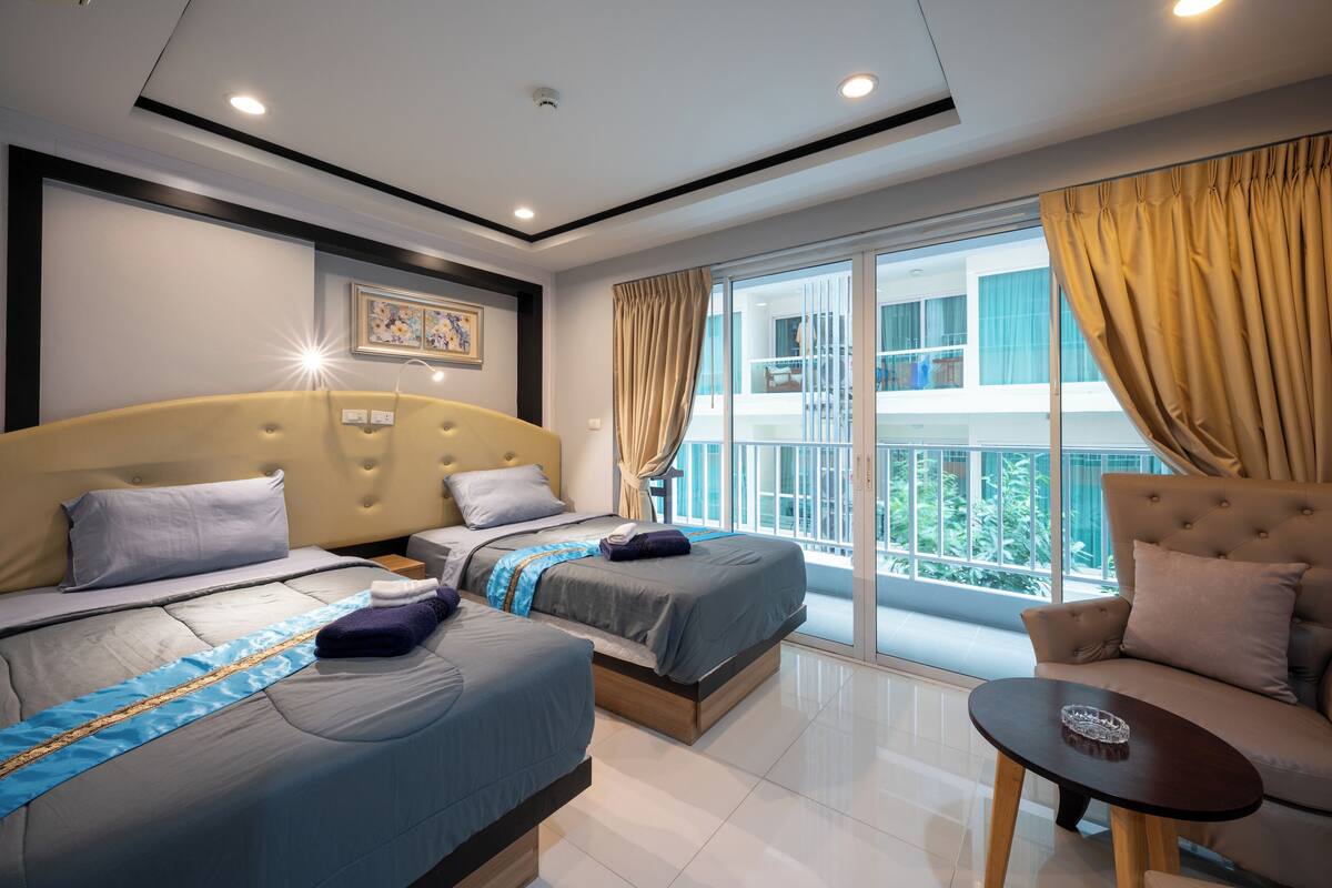 Habitación de hotel con dos camas, un sofá, una mesita y un balcón con cortinas.