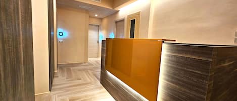 A hotel reception area with a wooden reception desk, a wooden floor, and a door in the background.