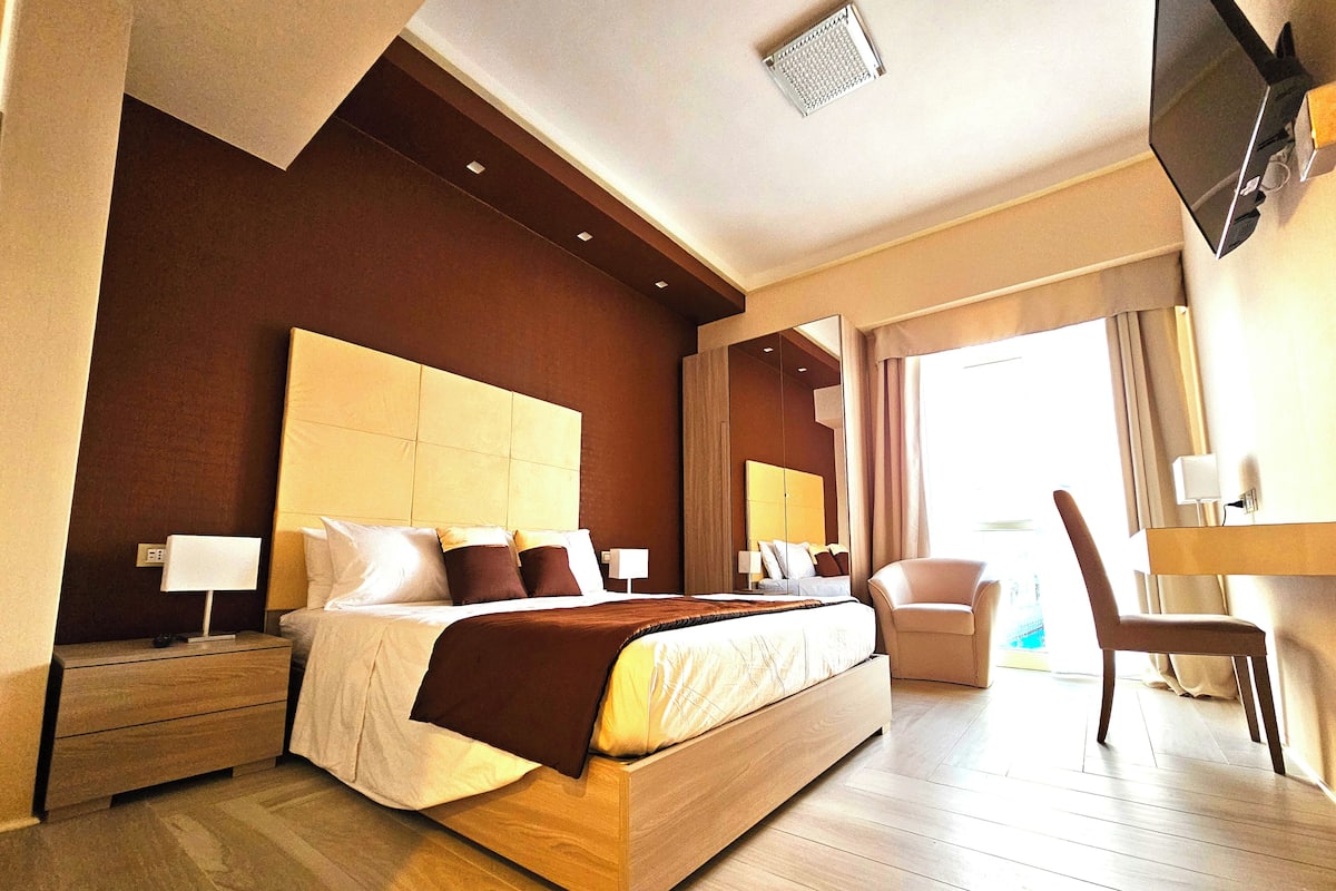 A modern hotel room with a large bed, bedside tables, a TV, and a chair.