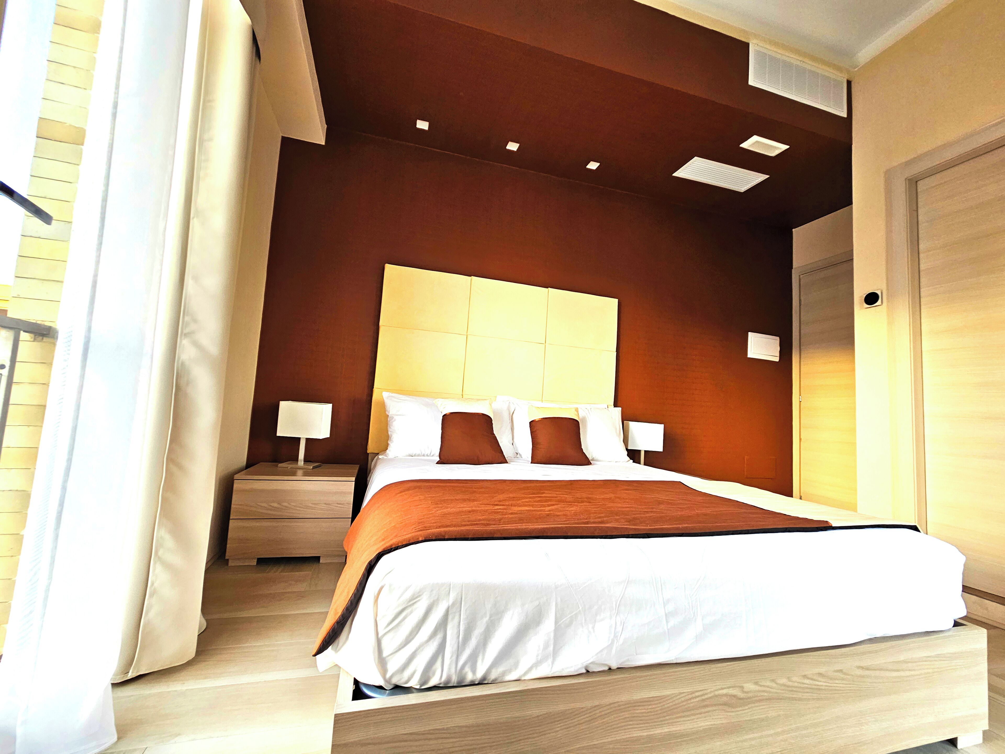 A hotel room with a large bed, two bedside tables, a headboard, and a door.