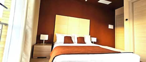 Una habitación de hotel con una cama grande, dos mesitas de noche, un cabecero y una puerta.