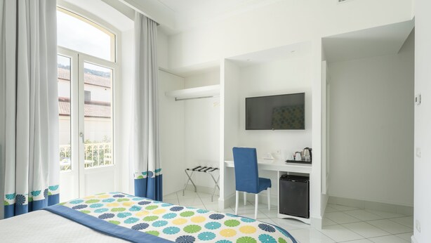 Habitación de hotel con cama, escritorio, silla, televisión y vistas al exterior.