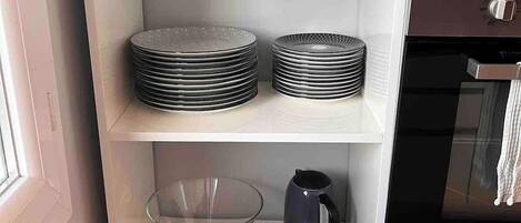 Una cocina con estantes blancos que sostienen tazones, platos y un hervidor.