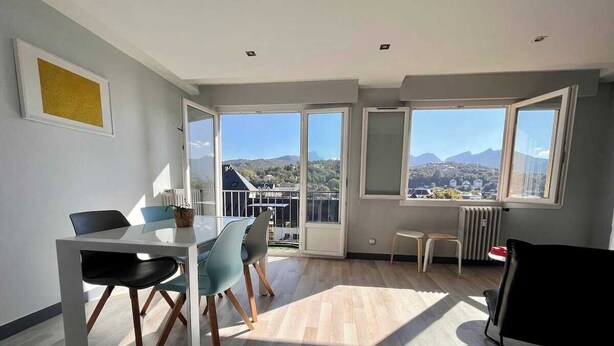 A spacious room with a dining area, a black chair, and a view of the mountains through large windows. - Beautiful modern 7th floor apartment with panoramic views  (Chambéry)