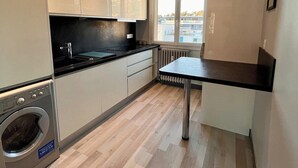 A modern kitchen with white cabinets, a built-in washing machine, and a view through the window. - Beautiful modern 7th floor apartment with panoramic views  (Chambéry)