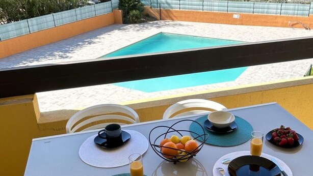 En balkong med ett bord dukat för frukost, med utsikt över en swimmingpool.