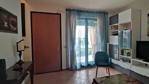Uma sala de estar com televisão, uma cadeira, estante de livros e uma porta.