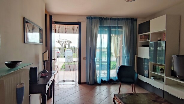 Sala de estar com televisão, área de jantar com mesa e cadeiras, cozinha com fogão e uma tigela, e varanda com vista para o exterior.