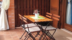Uma mesa de jantar de madeira com cadeiras, rodeada por plantas em vasos sobre prateleiras, sob uma estrutura de teto de madeira.