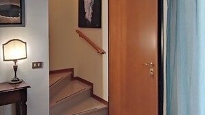 Um corredor com escadas, uma porta, um abajur e um quadro na parede.
