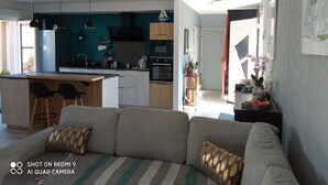 A modern kitchen with a central island, a dining area with chairs, a sofa with patterned cushions, and a hallway leading to another room.