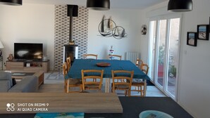 A modern living room with a TV, fireplace, and dining area with wooden chairs and a blue tablecloth.