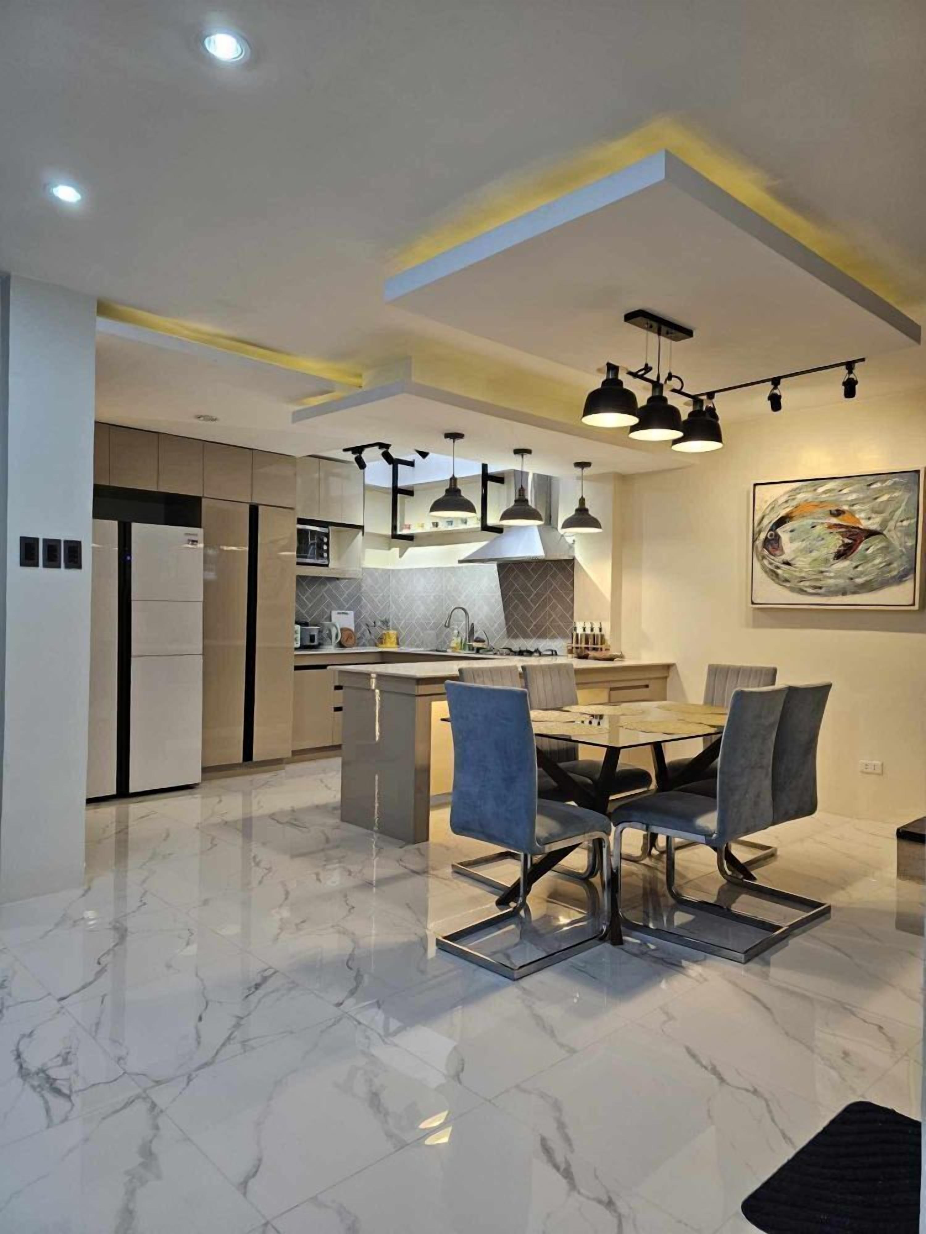 Een moderne keuken met een centraal eiland, hanglampen en een eetgedeelte met een marmeren vloer.
