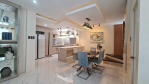 Una cucina moderna con zona pranzo, caratterizzata da un pavimento in marmo, illuminazione a sospensione e un grande quadro a parete.