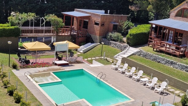 A pool area with lounge chairs, a small building with a balcony, and a stone wall. - CasaAlpina (Tandil)
