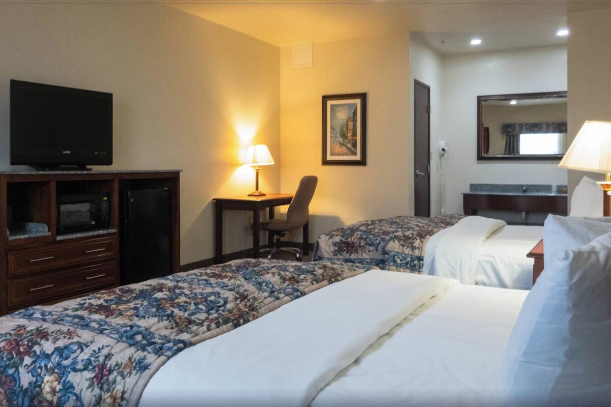 A hotel room with two beds, a desk, a television, and a chair.
