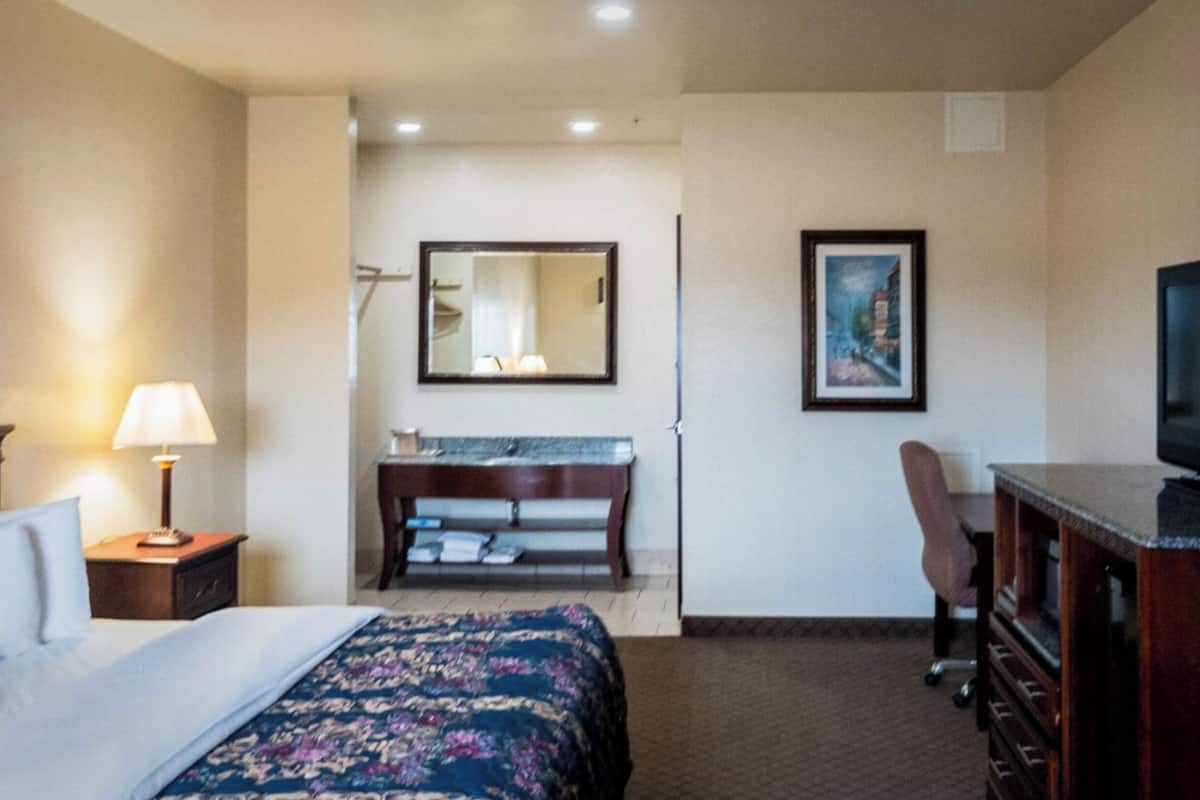 A hotel room with a bed, a desk, a television, a bathroom with a mirror, and a framed picture on the wall.