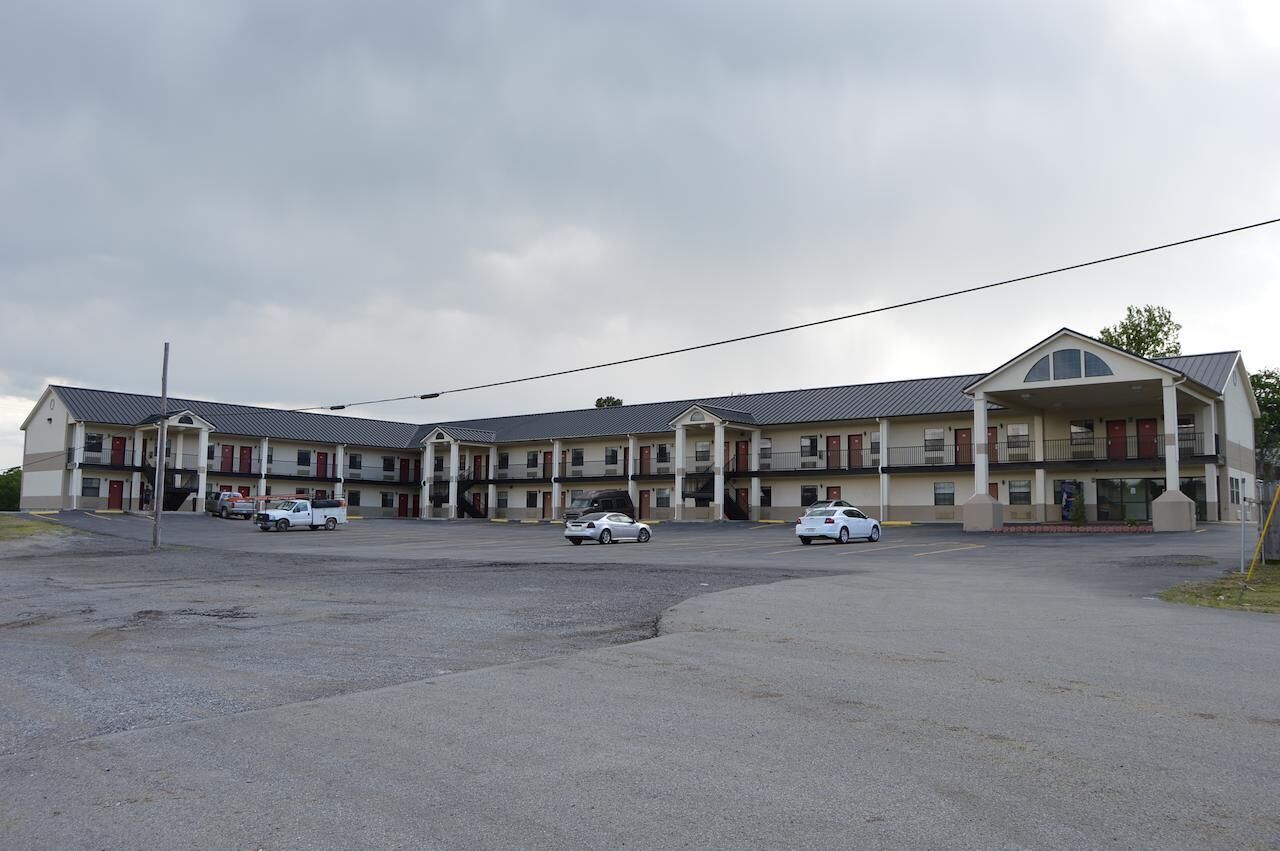 A multi-story motel with a central courtyard, featuring a parking lot with several cars.