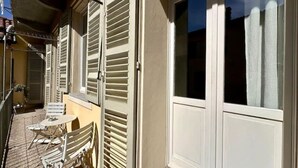 A balcony with white shutters, a small table, and two chairs. - Don Bosco House (Chieri)