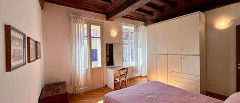 A bedroom with a wooden ceiling, a bed with a pink bedspread, a desk, and a wardrobe.