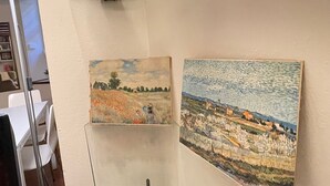 Deux tableaux sont accrochés au mur : un paysage représentant des arbres et un champ, et un paysage marin avec un bateau.