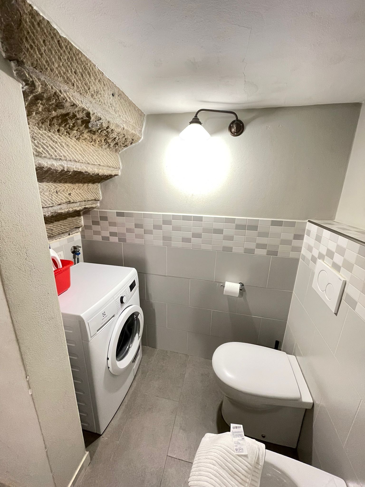 Une petite salle de bain équipée d’un lave-linge, de toilettes et d’un mur recouvert de carreaux.