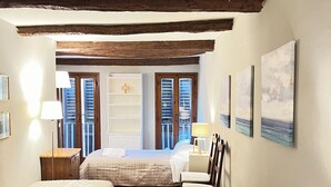 Une chambre d’hôtel avec deux lits, des poutres apparentes, une fenêtre avec volets et des œuvres d’art accrochées au mur.