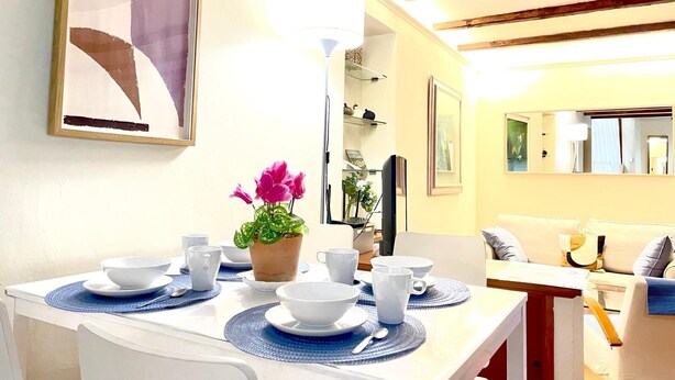 Un coin repas avec une table dressée pour quatre personnes, une plante en pot et un tableau accroché au mur.