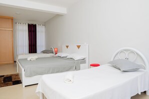 A hotel room with two single beds, a red stool, a white headboard, and a wooden wardrobe.