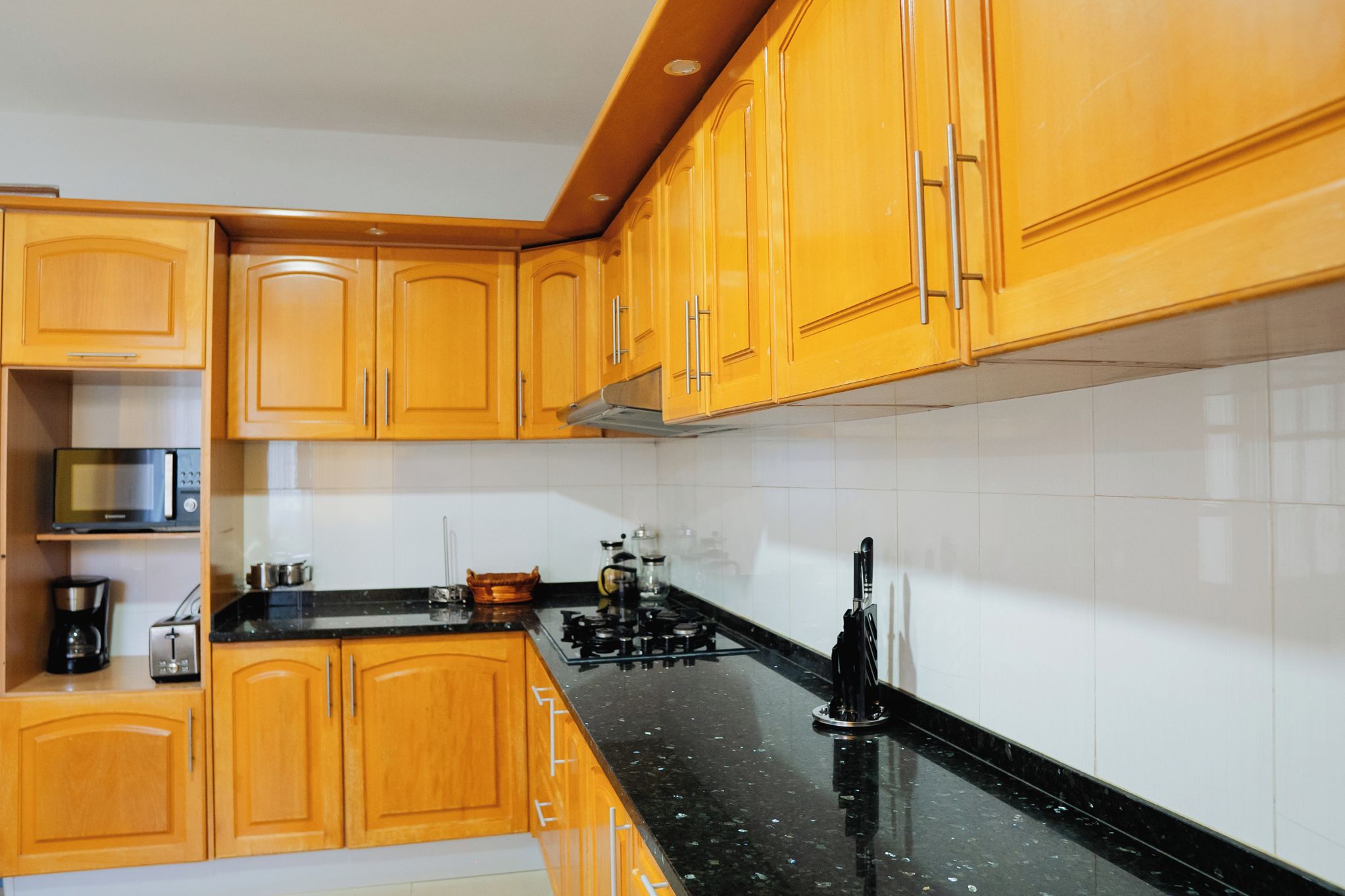 Una cocina con armarios de madera, encimera negra, estufa y microondas.