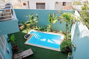 A rooftop pool with surrounding greenery and a small seating area.