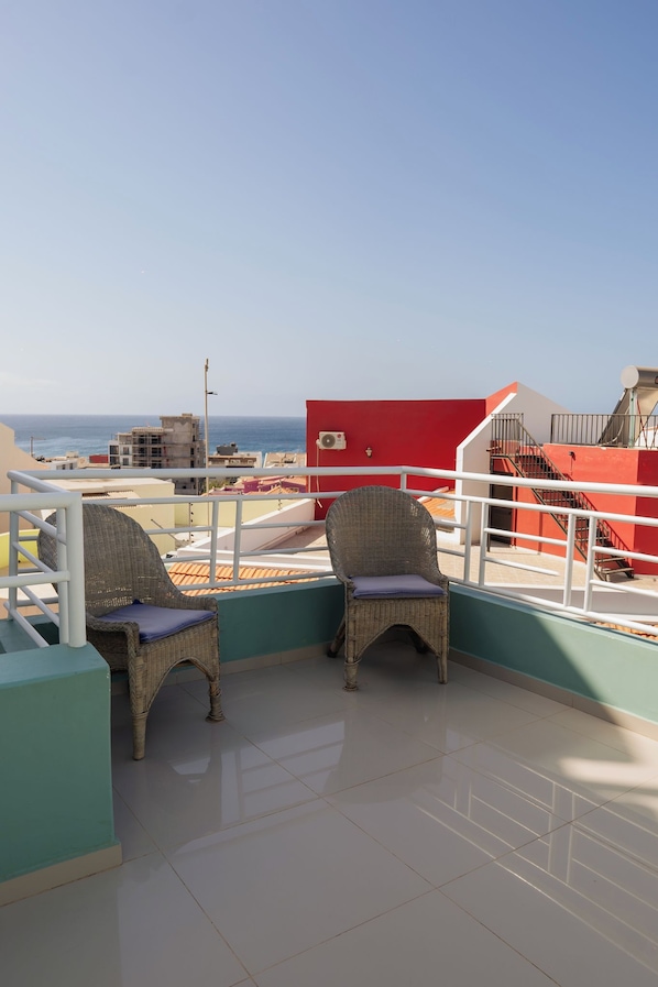 A balcony with two wicker chairs, a red wall, and a view of the sea.