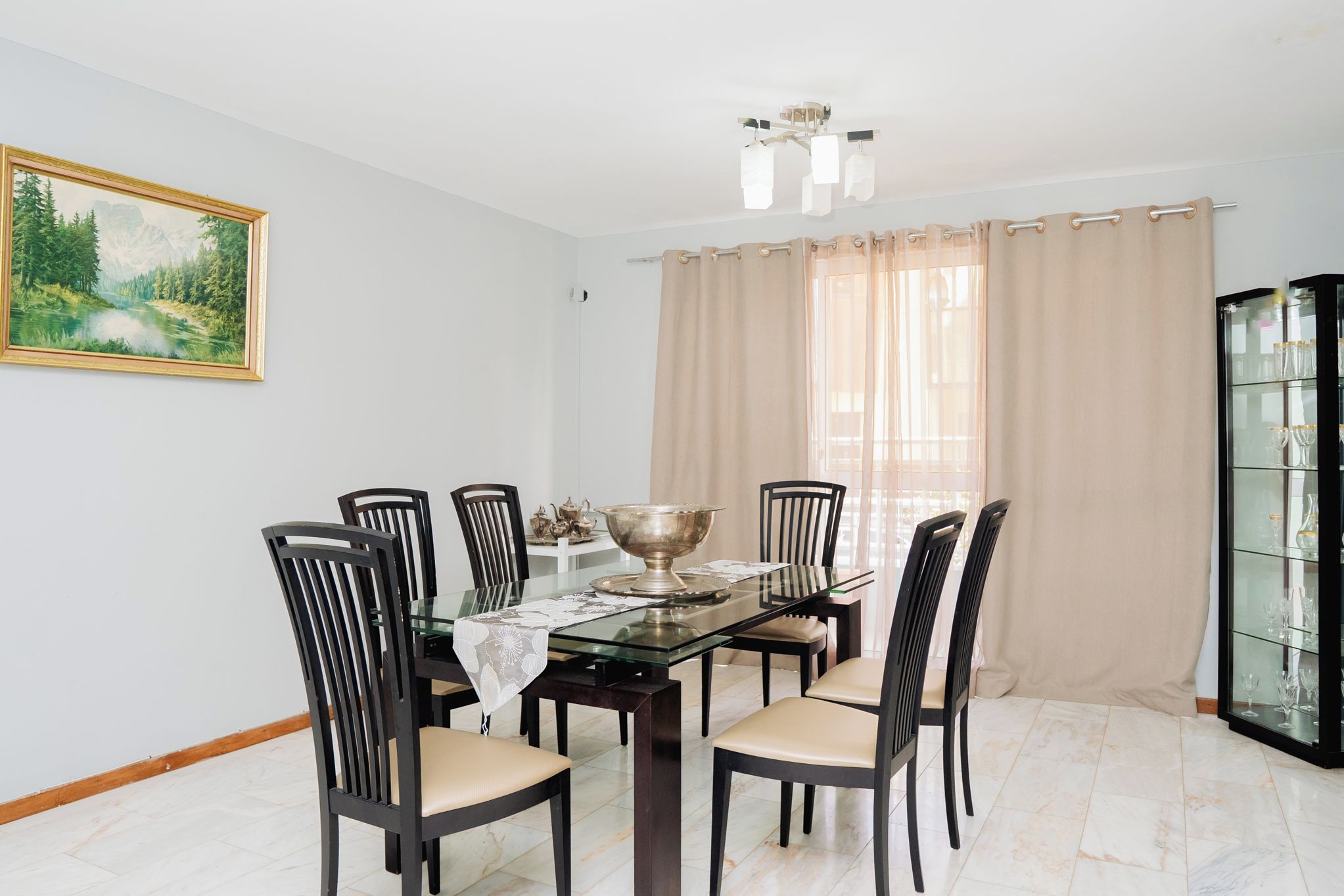 Un comedor con mesa de vidrio, seis sillas, un cuenco decorativo y un cuadro en la pared.