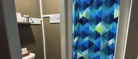 A bathroom with a white toilet, a shower curtain with a geometric pattern, a sign on the wall, and a small rug on the floor.