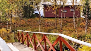 Un pontile in legno con ringhiera rossa conduce a una baita circondata da fogliame autunnale.