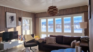 Un accogliente soggiorno con soffitto in legno, un'ampia finestra con vista innevata, un divano, un tavolino da caffè e una televisione.