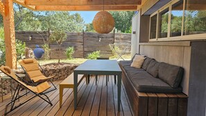 A wooden deck with a table and chairs, a cushioned bench, and a hanging light fixture.