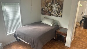 A bedroom with a bed, a ceiling fan, a zebra painting, and a wooden floor.