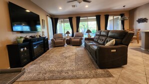 A living room with a flat-screen TV, leather sofas, a ceiling fan, and a large window with curtains. - Anthem Family getaway (Anthem)