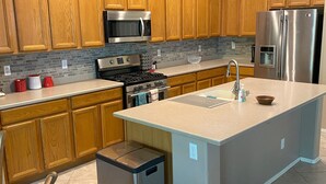 A modern kitchen with wooden cabinets, stainless steel appliances, and a large island. - Anthem Family getaway (Anthem)