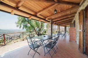 Un patio exterior con techo de madera, paredes de piedra y vistas al paisaje.