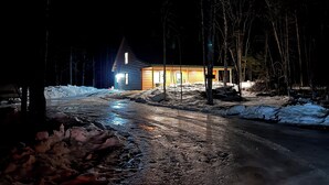 Una baita con interni illuminati, circondata da terreno e alberi innevati.